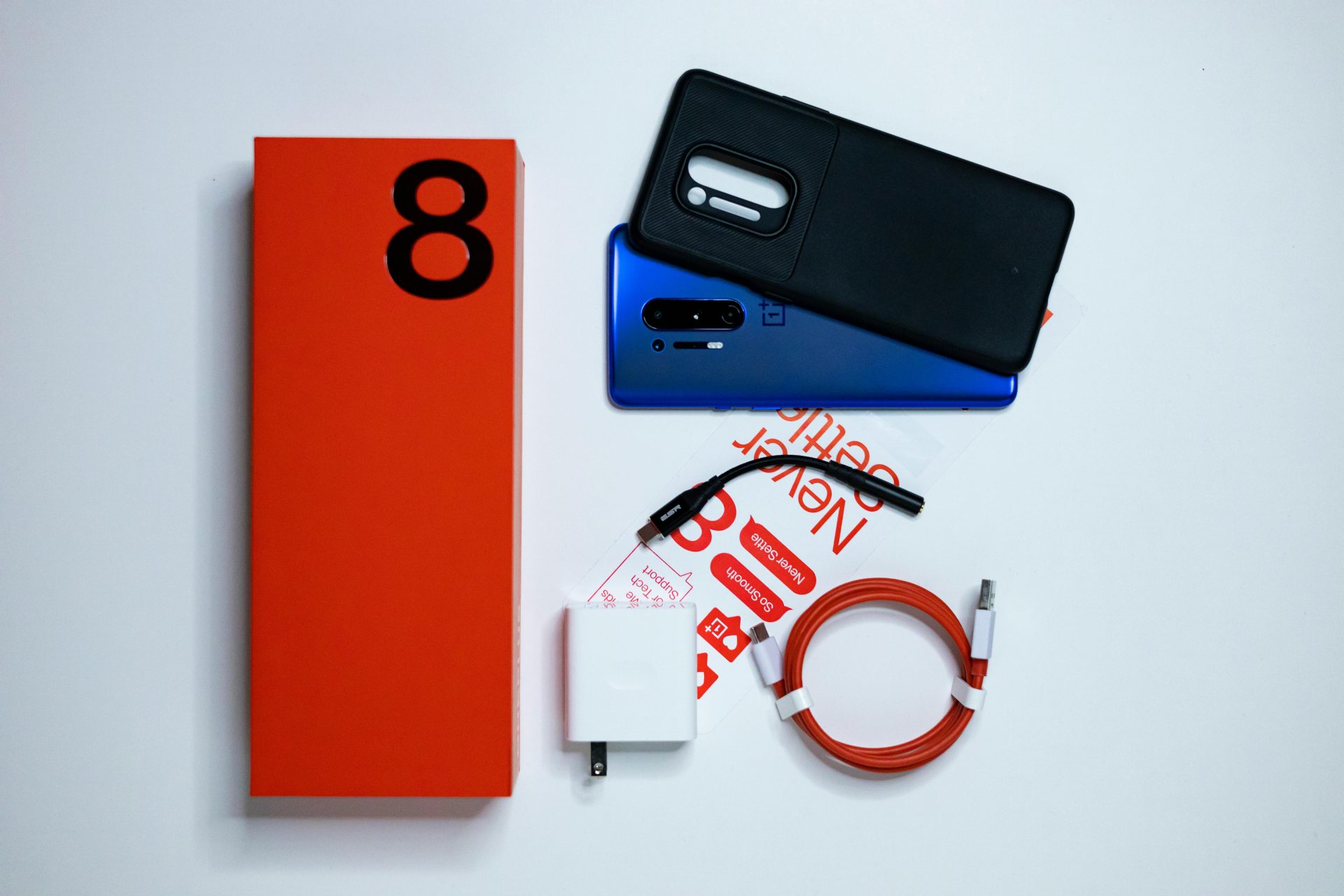Flat lay photo of OnePlus 8 smartphone unboxing with accessories on a white background.